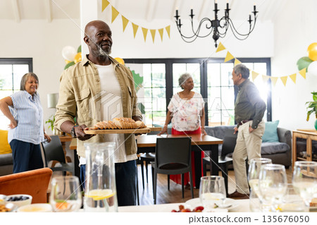Elderly man serving bread at family gathering, smiling and enjoying celebration 135676050