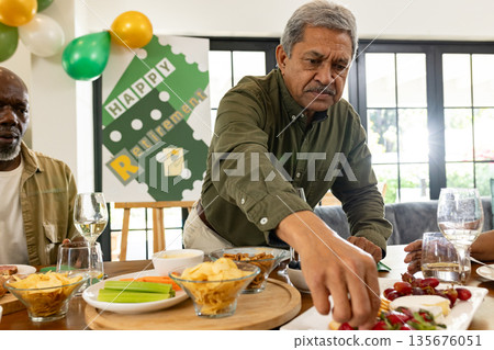 Man enjoying retirement party, reaching for snacks at festive gathering table 135676051