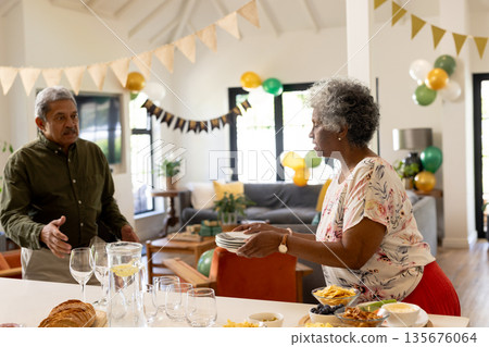 Elderly couple preparing for celebration, arranging dishes and decorations at home Elderly couple preparing for celebration, arranging dishes and decorations at home 135676064
