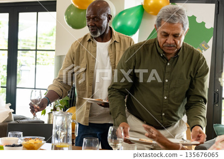 African American man holding wine glass and plate, preparing for celebration at home 135676065