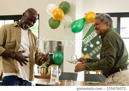Two men laughing and holding glasses at retirement party with balloons Two men laughing and holding glasses at retirement party with balloons 135676072