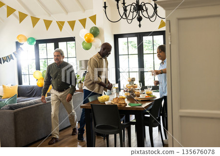 Friends preparing festive table with snacks and drinks for indoor celebration Friends preparing festive table with snacks and drinks for indoor celebration 135676078