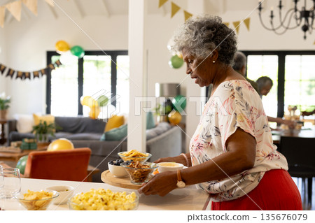 Elderly woman preparing snacks for family celebration in decorated living room 135676079