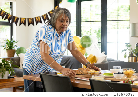 African American woman preparing food on table for retirement celebration at home African American woman preparing food on table for retirement celebration at home 135676083
