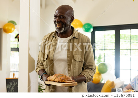 Smiling man holding bread on wooden board at festive home gathering 135676091