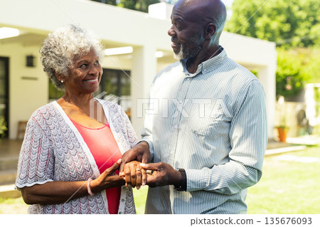 Elderly couple holding hands and smiling warmly in sunny garden 135676093