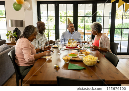 Senior friends celebrating birthday at home, enjoying cake and conversation together Senior friends celebrating birthday at home, enjoying cake and conversation together 135676100