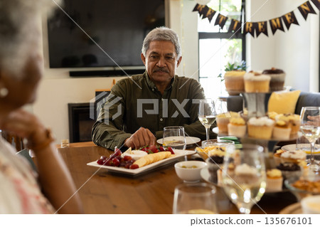 Family gathering around table enjoying food and drinks at home celebration 135676101
