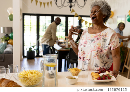 African American woman joyfully singing at family celebration with snacks on table 135676115