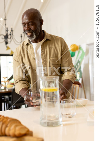 Smiling man in kitchen pouring water into glass during morning celebration Smiling man in kitchen pouring water into glass during morning celebration 135676119