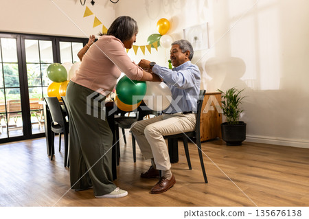 Elderly couple joyfully decorating room with colorful balloons for celebration Elderly couple joyfully decorating room with colorful balloons for celebration 135676138