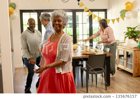 Celebrating at home, African American woman in red dress with friends, smiling joyfully 135676157