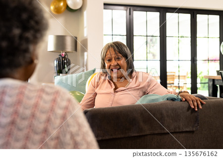 African American woman sitting on sofa at home, smiling and talking with friend 135676162
