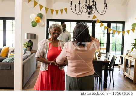 Elderly woman in red dress celebrating birthday at home with family, smiling warmly 135676166
