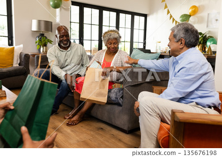 Sharing laughter, elderly friends exchanging gifts in cozy living room celebration Sharing laughter, elderly friends exchanging gifts in cozy living room celebration 135676198
