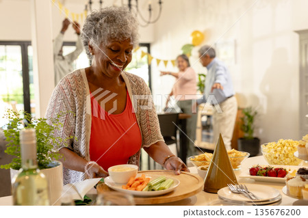 Elderly woman serving snacks at family gathering, smiling and enjoying celebration 135676200