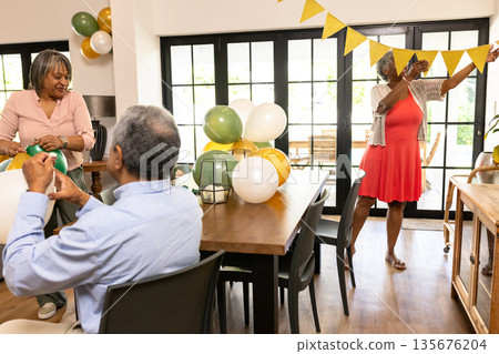 Senior friends hanging bunting and arranging balloons for celebration at home Senior friends hanging bunting and arranging balloons for celebration at home 135676204