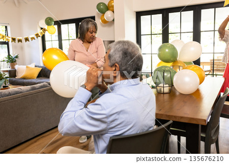 Senior couple decorating living room with colorful balloons for festive celebration Senior couple decorating living room with colorful balloons for festive celebration 135676210