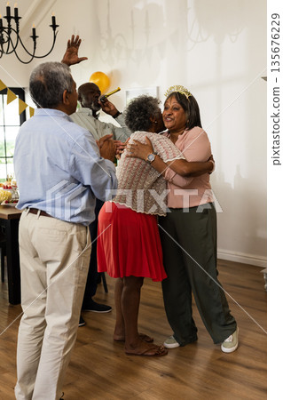 Elderly friends celebrating birthday with hugs and laughter at home party Elderly friends celebrating birthday with hugs and laughter at home party 135676229