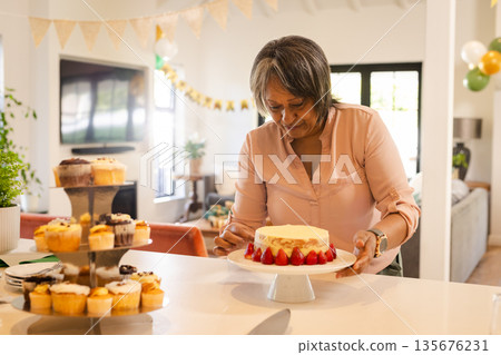 Woman decorating cake with strawberries in living room during celebration Woman decorating cake with strawberries in living room during celebration 135676231