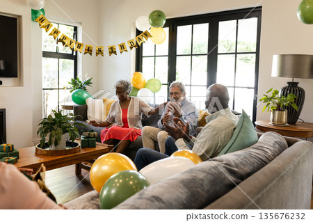 African American seniors celebrating birthday, having conversation in living room with balloons African American seniors celebrating birthday, having conversation in living room with balloons 135676232