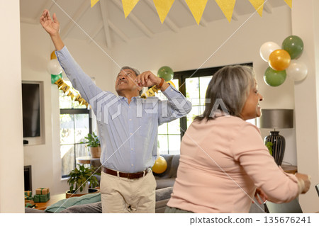 Elderly couple dancing joyfully at home during festive celebration with decorations Elderly couple dancing joyfully at home during festive celebration with decorations 135676241