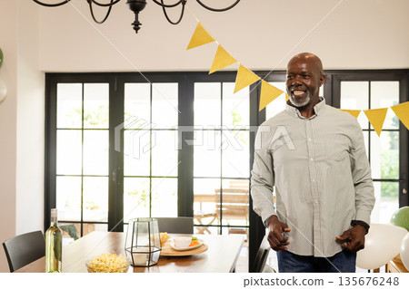 African American man celebrating at home, smiling near decorated dining table 135676248