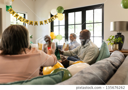 Celebrating birthday at home, diverse group enjoying drinks and laughter together 135676262