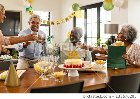 Family celebrating birthday with cake and gifts, raising glasses in living room 135676293