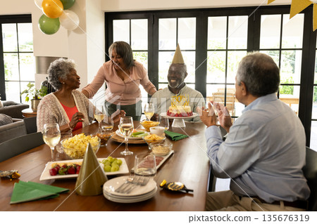 Family celebrating birthday with cake and laughter at home dining table Family celebrating birthday with cake and laughter at home dining table 135676319