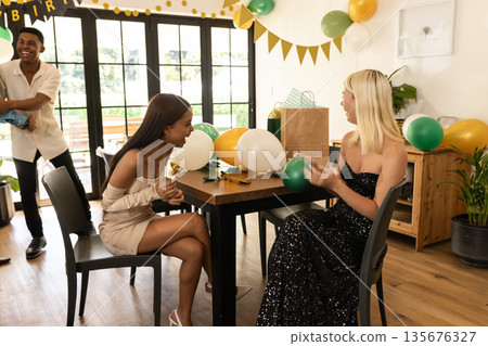 Friends celebrating birthday at home, smiling and decorating with balloons and gifts 135676327