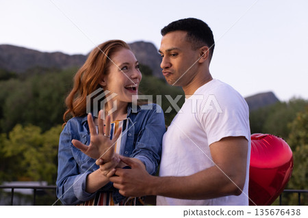 Young couple celebrating engagement outdoors, woman showing ring with excitement 135676438