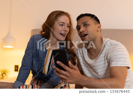 Young couple at home enjoying smartphone together, sharing joyful moment 135676445