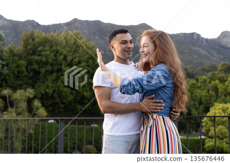 Young couple embracing outdoors, smiling and enjoying scenic mountain view 135676446
