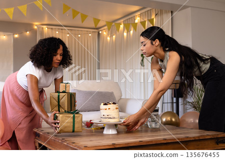 Friends decorating table with cake and gifts for celebration at home Friends decorating table with cake and gifts for celebration at home 135676455