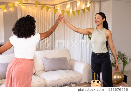 Friends celebrating at home, giving high five near cake and decorations Friends celebrating at home, giving high five near cake and decorations 135676456