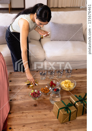 Woman arranging snacks and gifts on wooden table, preparing for celebration at home Woman arranging snacks and gifts on wooden table, preparing for celebration at home 135676461