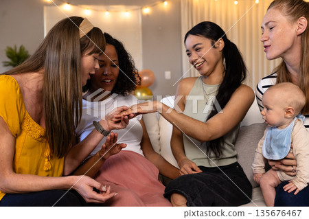 Women admiring engagement ring at home, celebrating joyful moment together 135676467
