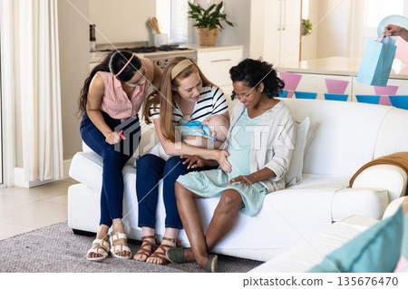 Women celebrating baby shower at home, smiling and sharing gifts on sofa Women celebrating baby shower at home, smiling and sharing gifts on sofa 135676470