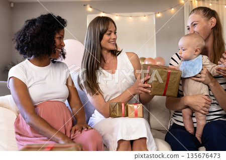 Women celebrating baby shower, giving gifts and smiling with joy at home Women celebrating baby shower, giving gifts and smiling with joy at home 135676473
