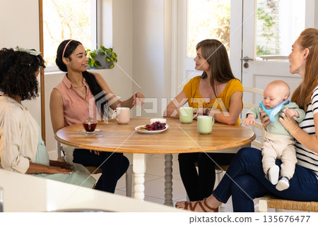 Women enjoying coffee and conversation at home, one holding baby 135676477