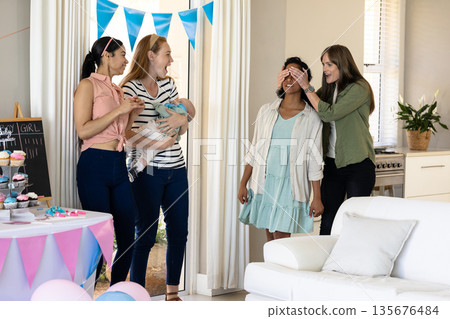 Women celebrating baby shower at home, smiling and enjoying festive decorations Women celebrating baby shower at home, smiling and enjoying festive decorations 135676484