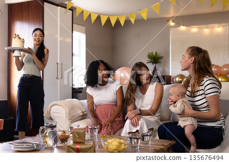 Bringing birthday cake, woman celebrating with friends and baby sitting on couch Bringing birthday cake, woman celebrating with friends and baby sitting on couch 135676494