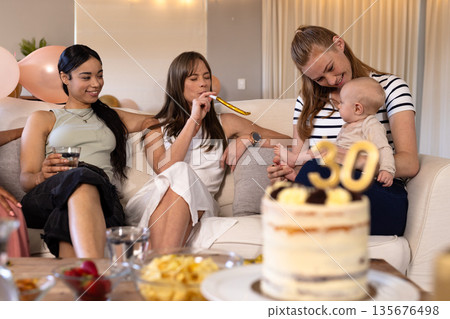 Celebrating birthday, women enjoying party with cake and baby on cozy sofa 135676498