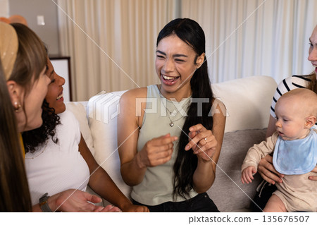 Friends laughing and bonding on couch while woman holds baby, enjoying time together 135676507
