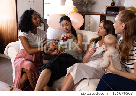 Women enjoying conversation and snacks on sofa during cozy indoor gathering 135676508