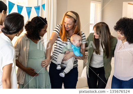 Friends celebrating baby shower, smiling and gathering around pregnant woman at home Friends celebrating baby shower, smiling and gathering around pregnant woman at home 135676524