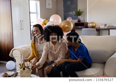 Celebrating at home, three women laughing and enjoying cake with balloons around Celebrating at home, three women laughing and enjoying cake with balloons around 135676527