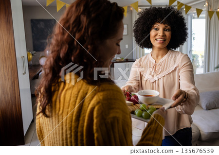 Smiling woman serving appetizers to friend at home during festive gathering Smiling woman serving appetizers to friend at home during festive gathering 135676539