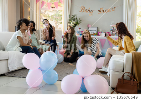 Women celebrating baby shower with balloons and laughter in cozy living room Women celebrating baby shower with balloons and laughter in cozy living room 135676549